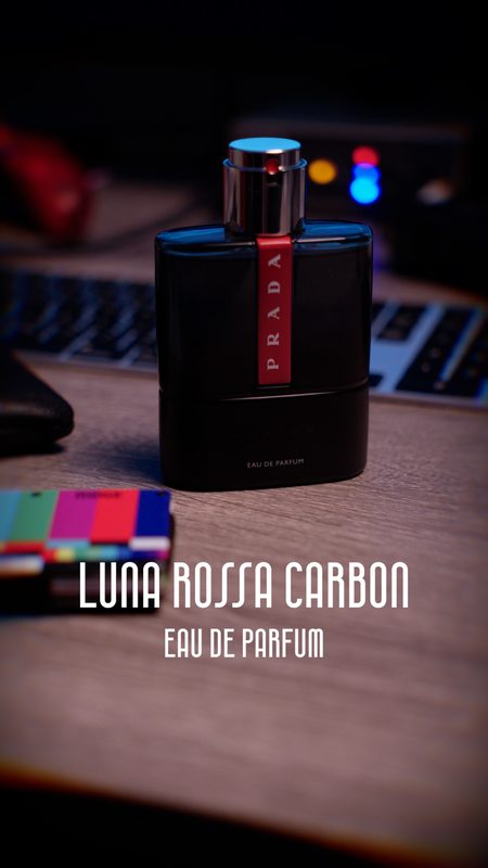 Prada Luna Rossa Carbon eau de parfum on a wooden desk with moody blue and red light — product photography